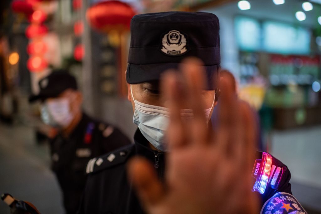 Un agente di polizia cerca di impedire a un fotoreporter di scattare foto, in una strada fuori da un complesso di centri commerciali a Pechino il 13 ottobre 2020. (Nicolas Asfouri/AFP via Getty Images)