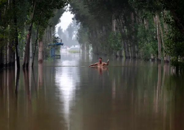 Un abitante del luogo gesticola mentre cammina tra le acque alluvionali profonde fino al petto in un'area vicino a Zhuozhou, nella provincia di Hebei, in Cina, a sud di Pechino, il 3 agosto 2023. (Kevin Frayer/Getty Images)