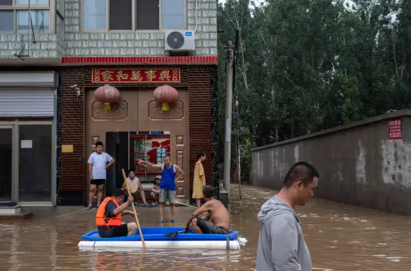 Residenti locali, alcuni su una barca di fortuna, parlano davanti alla loro casa in un'area inondata dalle acque vicino a Zhuozhou, nella provincia di Hebei, in Cina, a sud di Pechino, il 3 agosto 2023. (Kevin Frayer/Getty Images)