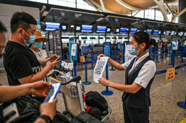 Passeggeri con mascherine controllano il loro codice sanitario con un foglio tenuto da un membro del personale aeroportuale (a destra) all'aeroporto internazionale di Pudong a Shanghai l'11 giugno 2020. (Hector Retamal/AFP via Getty Images)