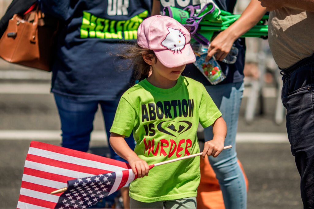 Una bambina di un gruppo cristiano evangelico indossa una maglietta pro-vita e porta una bandiera americana durante l'annuale La Pride Parade a West Hollywood, in California, il 9 giugno 2019. (DAVID MCNEW/Afp via Getty Images)