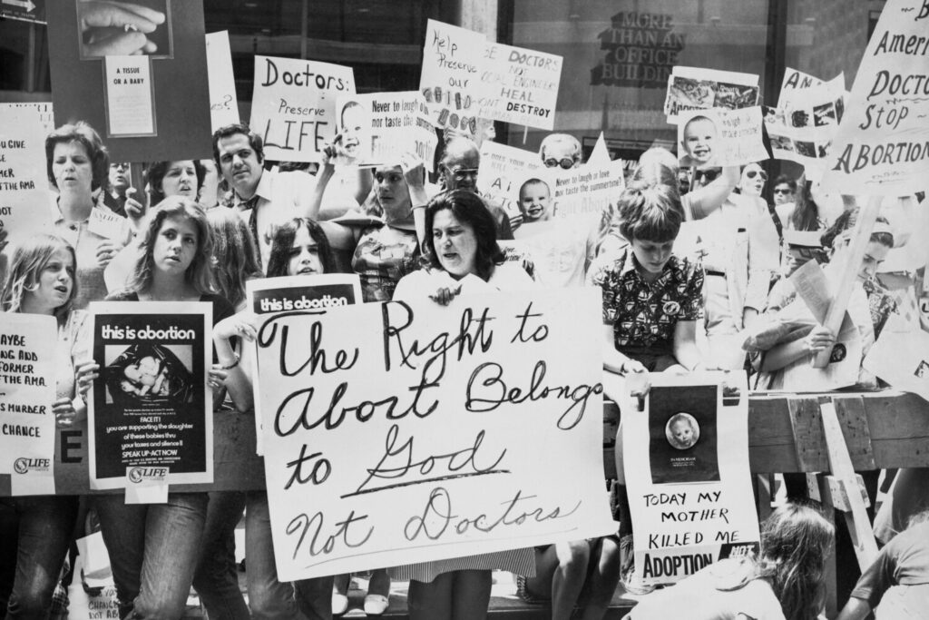 Attivisti pro-vita si riuniscono per protestare contro l'aborto fuori da un hotel dove si sta svolgendo il congresso annuale dell'American Medical Association a New York City, 1975 circa. (Peter Keegan/Authenticated News/Archive Photos/Getty Images)