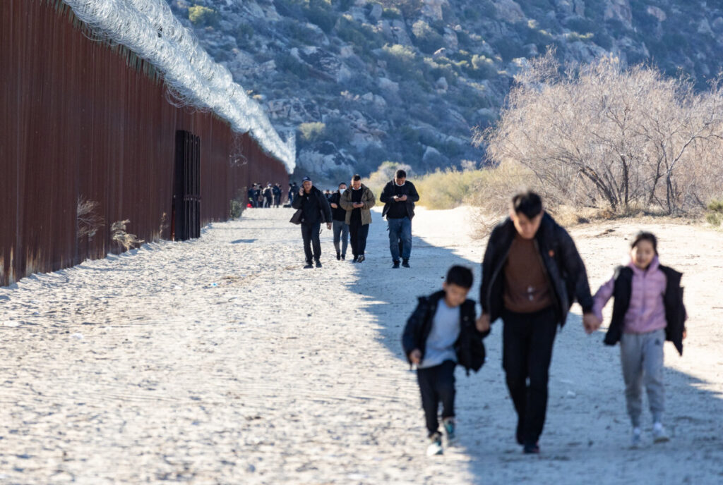 Migranti camminano lungo il lato statunitense del muro di confine degli Stati Uniti dopo aver attraversato un varco aperto a Jacumba, in California, il 6 dicembre 2023. (John Fredricks/Epoch Times)