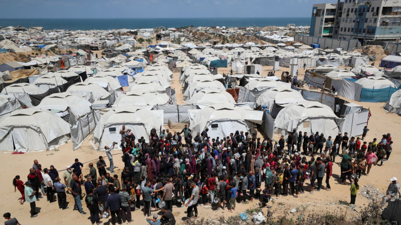 Palestinesi aspettano di ricevere cibo vicino alle tende dove si sono rifugiati dopo essere stati sfollati a causa dell'offensiva militare israeliana, a Gaza City, 28 maggio 2025. (REUTERS/Mahmoud Issa)